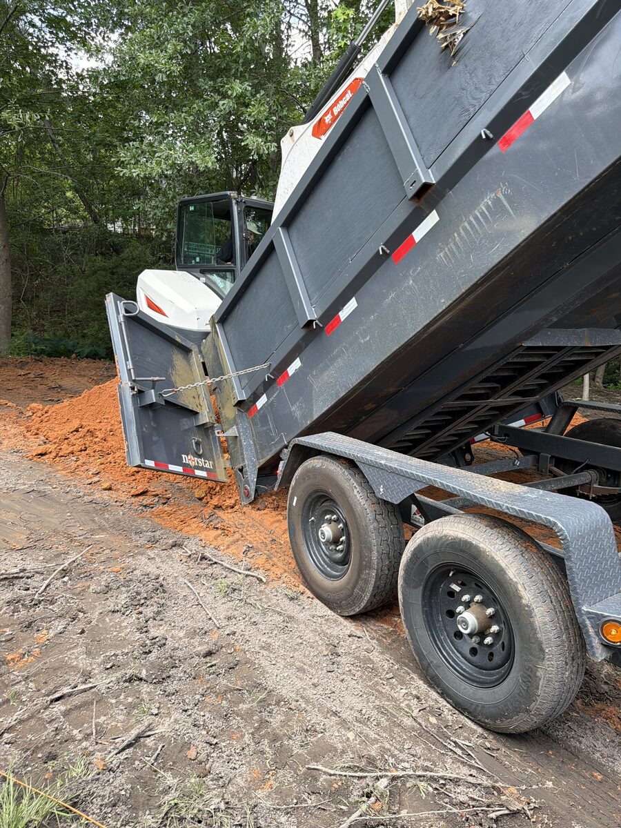 Black dump trailer raised beside Marucci Enterprises equipment during debris unloading