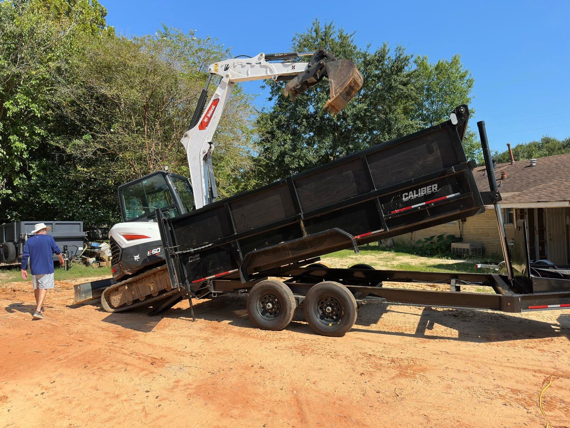 Marucci Enterprises excavator loading a raised black dump trailer at a Gulf Coast jobsite